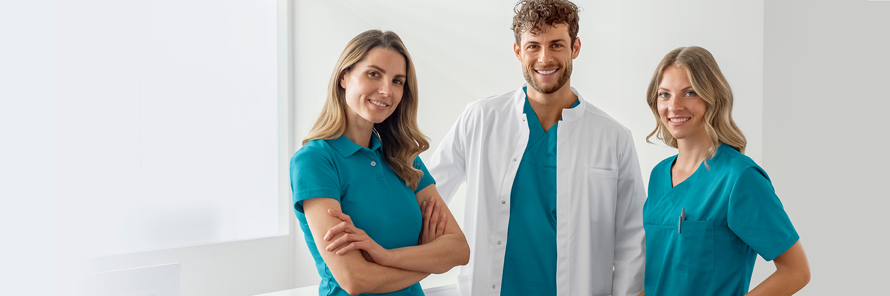 Een man in een doktersjas en turquoise jurk en twee vrouwen in poloshirts en turquoise jassen in een medisch kantoor